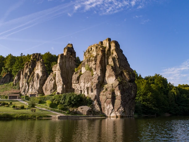 Naturdenkmal Externsteine: Majestätische Sandsteinfelsen am Teich mit Wäldern im Hintergrund.