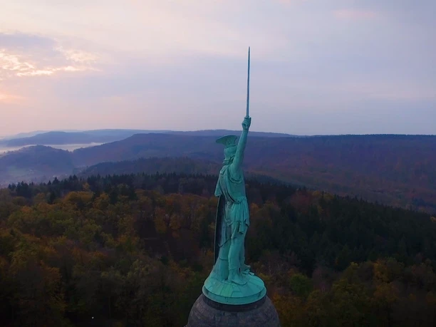 Hermannsdenkmal Blick auf die eindrucksvolle Hermannsstatue, umgeben von bewaldeter Hügellandschaft bei Dämmerung.