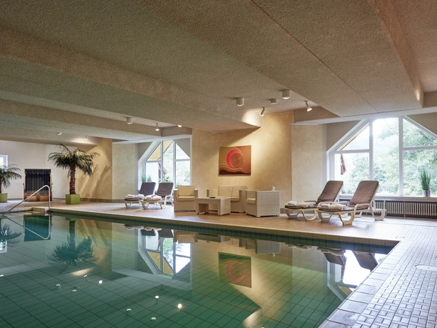 Schwimmbad Hotel Bärenstein Innenansicht eines Hotelhallenbades mit Liegestühlen, Palmen, einem Wandbild und großen Fenstern.