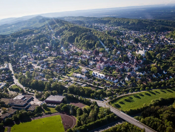 Luftaufnahme von Oerlinghausen mit grünen Hügeln, dichter Bebauung und umliegenden Wäldern bei Sonnenschein.