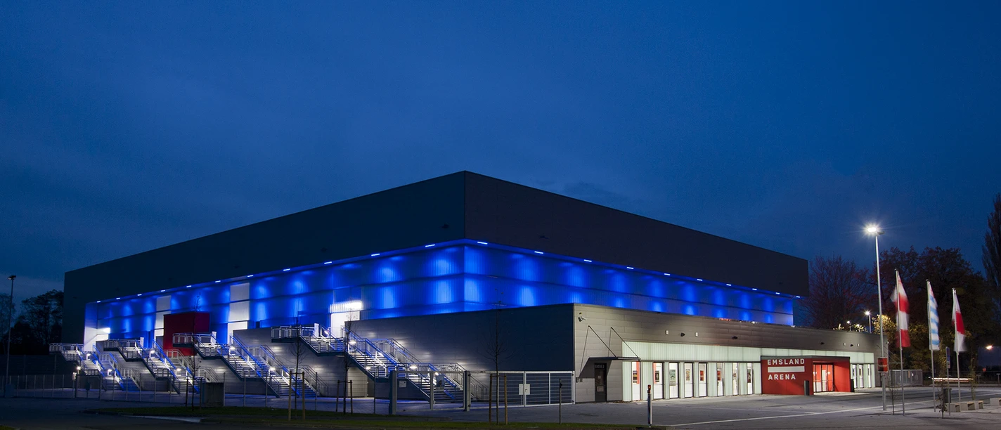 EmslandArena Modernes Veranstaltungsgebäude mit blauer Fassadenbeleuchtung und rotem Eingang bei Nacht