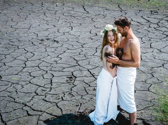 bad-driburg-moor-bad-driburger-touristik-gmbh-daniel-winkler-53 Ein Paar steht eingewickelt in weiße Tücher auf rissigem Boden und lacht freudig in die Kamera.