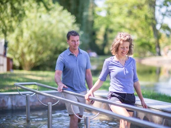 Kneipp-Tretbecken Zwei Personen nutzen ein Kneipp-Tretbecken im Freien bei sonnigem Wetter, umgeben von Natur.