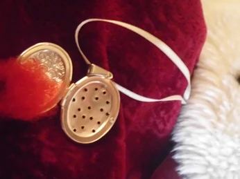 Historische Flohfalle Silberne, geöffnete Flohfalle mit rotem Wollbüschel auf samtigem roten Hintergrund.