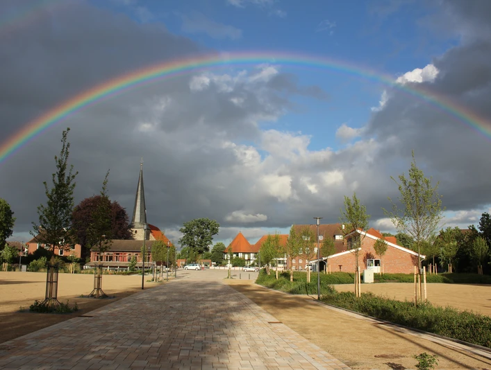 Stadtplatz Rehburg Ein weitläufiger Stadtplatz in Rehburg unter einem eindrucksvollen Regenbogen, mit Kirche und Häusern.