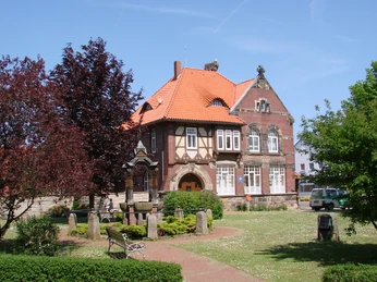 Alte Schule Rehburg Backsteingebäude mit Fachwerkelementen, umgeben von Bäumen und einer gepflasterten Gartenanlage.