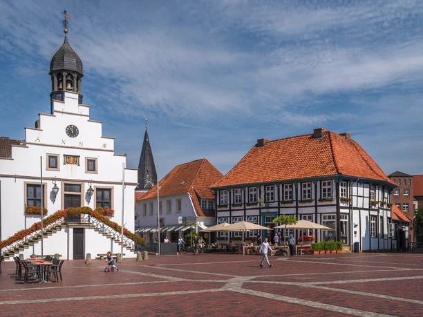 Historischer Marktplatz in Lingen mit Rathaus, Fachwerkhäusern und Caféterrasse bei Sonnenschein.