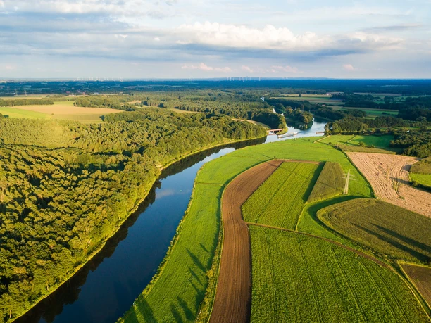 Luftaufnahme der Ems bei Lingen mit Feldern, Wiesen und Waldgebieten unter blauem Himmel.