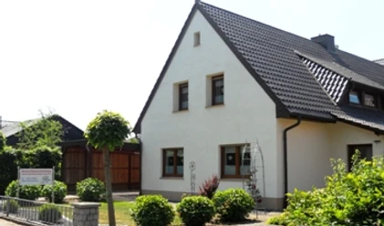 Helles Wohnhaus mit Satteldach, gepflegtem Vorgarten und angrenzender Einfahrt im Grünen.