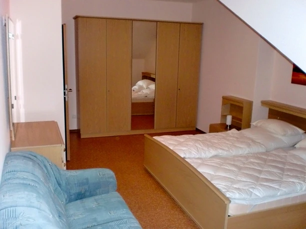 Ferienhof_Huesers_Haar_Haren.JPG Helles Schlafzimmer mit Doppelbett, Spiegelschrank, Nachttischen und hellblauer Couch unter Schräge.