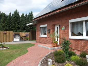 Ferienwohnung_Angelikas_Ferienparadies_-_Haseluenne-Huelsen.jpg Rotes Backsteinhaus mit Solardach, gepflegtem Garten, Gartenmöbeln und Blick auf grüne Bäume.