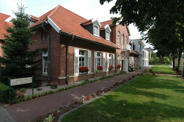 Backsteinhaus mit rotem Dach, weißen Fensterläden und Blumenkästen am Weg mit bepflanztem Rand