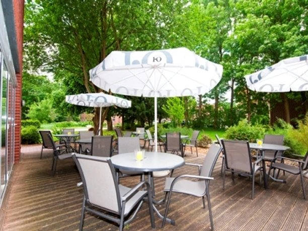 HotelAquamarin_PapenburgDraussen.JPG Sonnenterrasse des Hotels mit Tischen, Stühlen und weißen Sonnenschirmen im grünen Gartenbereich.