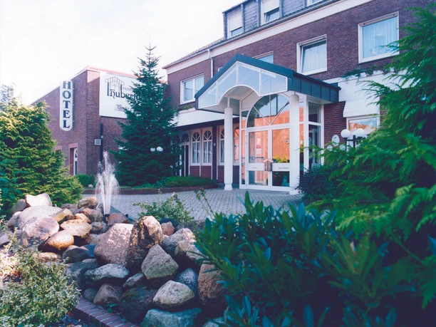 H_Hubertushof_Lingen_mini.jpg Eingangsbereich des Hotels Hubertushof in Lingen mit Glasvordach, Natursteinbrunnen und grüner Bepflanzung.