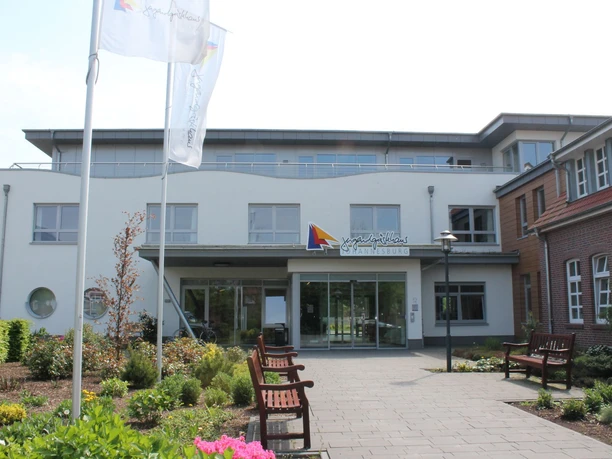 Jugendgaestehaus_Johannesburg_in_Papenburg_-_Haupteingang_klein.jpg Moderner Eingangsbereich des Jugendgästehauses Johannesburg mit Blumenbeeten und Sitzbänken.