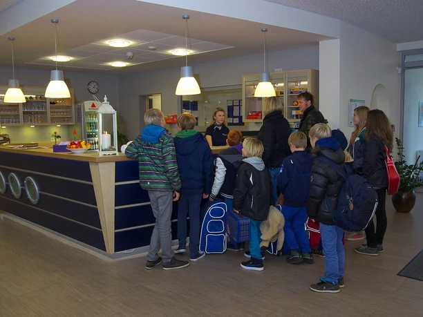 Jugendgaestehaus_Johannesburg_in_Papenburg_Check-In_Rezeption.jpg Kindergruppe mit Begleitpersonen steht in der hellen Rezeption des Jugendgästehauses beim Check-in.
