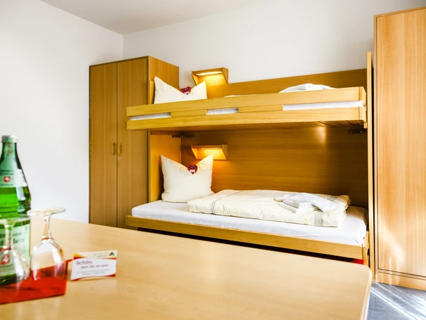 lingen_20150521_0130 Zweibettzimmer mit Etagenbett, Holzmöbeln, hellem Licht und Wasserflasche auf dem Tisch.