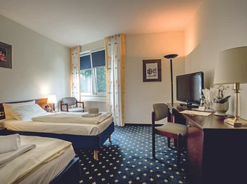 Zimmer_-_Parkhotel_Papenburg.jpg Helles Hotelzimmer mit zwei Einzelbetten, Schreibtisch, Fernseher, Sessel und großem Fenster.