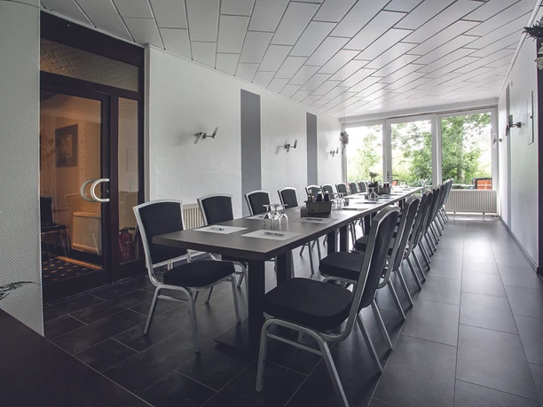Konferenzraum_-_Parkhotel_Papenburg.jpg Heller Konferenzraum mit langer Tischreihe, schwarzen Stühlen und großen Fenstern zum Park.
