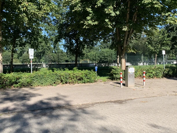 Womo Stellplatz Lingenerstr. Gepflasterter Platz mit Bäumen, Parkflächen für Wohnmobile und Versorgungssäule am Straßenrand.