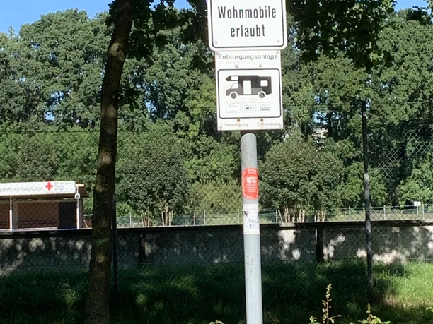 Womo Stellplatz Lingenerstr. 1 Verkehrsschild mit Hinweis auf erlaubte Wohnmobile und Entsorgungsanlage vor grünem Hintergrund.