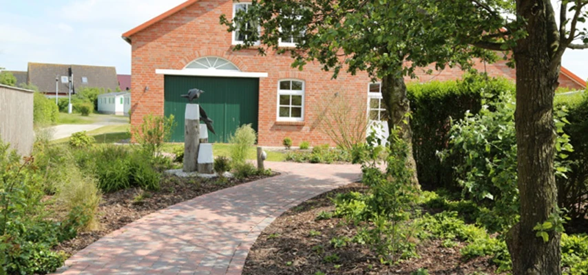 Camping am Deich in Krummhörn-Upleward Backsteingebäude am Deich mit grünem Tor, bepflanztem Gartenweg und Bäumen im Vordergrund