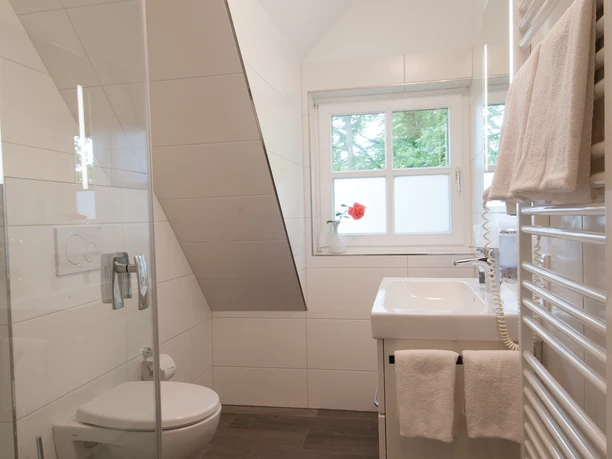 Badezimmer Helles, weiß gefliestes Badezimmer mit Glasdusche, WC, Waschbecken und Fenster.