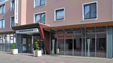 Hoteleingang mit Glasfront und Vordach, modernes Design mit schlichten Linien und klarer Struktur.