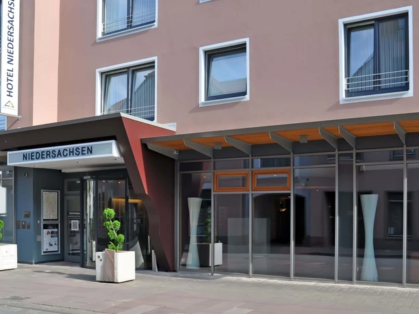 Hoteleingang mit Glasfront und Vordach, modernes Design mit schlichten Linien und klarer Struktur.