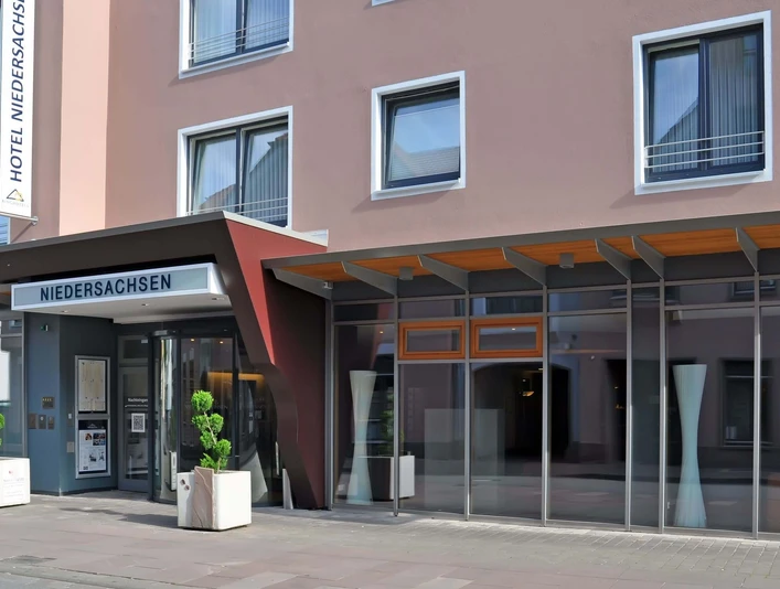 Hoteleingang mit Glasfront und Vordach, modernes Design mit schlichten Linien und klarer Struktur.