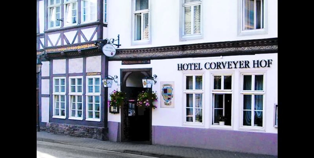 hotel-corveyerhof-hausansicht Fachwerkhaus mit Schild "Hotel Corveyer Hof" an der Fassade, Fenster mit Blumenkästen dekoriert.