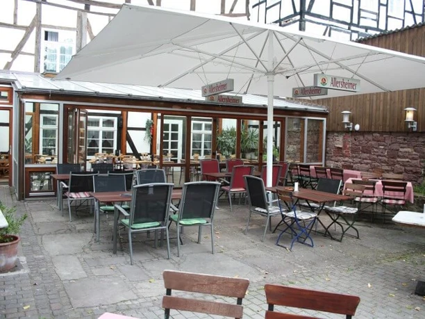 hotel-corveyerhof-biergarten Biergarten mit verschiedenen Holztischen und -stühlen, überdacht von großen Sonnenschirmen.