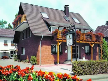 pension-zurweser-hausansicht Mehrstöckiges Gästehaus mit blühenden Balkonpflanzen und gepflegtem Vorgarten in einer ruhigen Wohngegend.