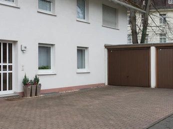 fewo-startpunkt1-garage Zweistöckiges Gebäude mit hellem Putz, daneben braune Doppelgarage, bepflanzte Blumenbehälter vorn.