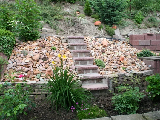 fewo-unterlaerchen-garten Steintreppe führt durch blühenden, bepflanzten Hang mit bunten Steinen in einem Garten.