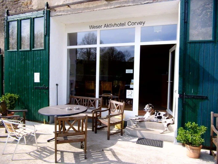 weseraktivhotel-eingang Eingangsbereich des Weser Aktivhotels Corvey mit Sitzmöglichkeiten und einem Hund auf der Treppe.
