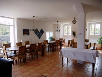 Heller Gruppenraum mit Holztischen und Stühlen, dekorativen Gemälden, Kronleuchtern und Pflanzen.