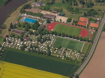 wesercamping-luftbild Luftbild eines Campingplatzes an der Weser mit angrenzendem Sportplatz und Schwimmbad, umgeben von Feldern.