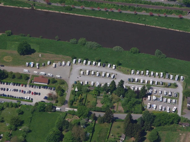 wohnmobil-flossplatz-luftbild Luftaufnahme eines Wohnmobil-Stellplatzes am Fluss mit geparkten Fahrzeugen und angrenzenden Grünflächen.