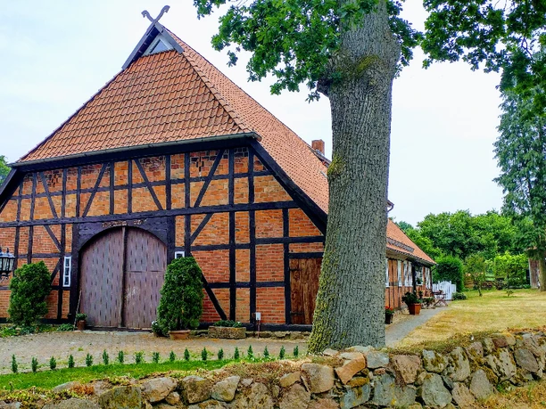 Außenansicht Traditionelles rotes Fachwerkhaus mit großem Dielentor und Garten hinter einer Natursteinmauer.