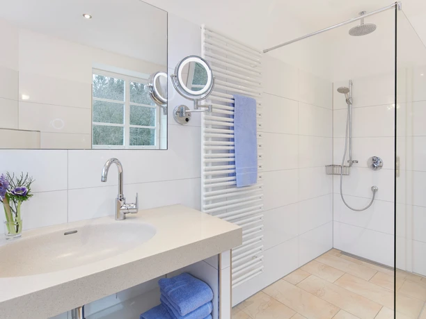 Badezimmer Helles Badezimmer mit ebenerdiger Glasdusche, großem Waschtisch und blauen Handtüchern.