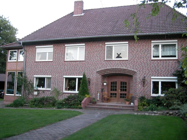 Außenansicht Großes Backsteinhaus mit Ziegeldach, Rasen und gepflastertem Weg zur Holztür.