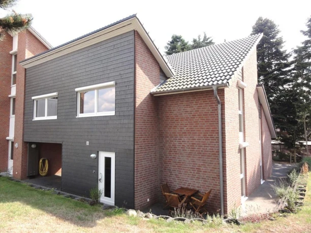 Außenansicht Ferienhaus mit rotem Backstein, dunkler Fassade und kleiner Terrasse im Grünen.