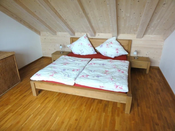 Schlafzimmer Schlafzimmer unter hölzerner Dachschräge mit Holzdoppelbett und geblümter Bettwäsche.