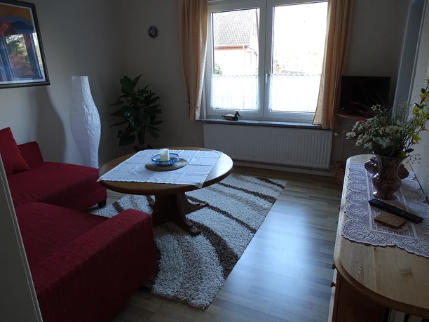 Wohnzimmer Helles Wohnzimmer mit rotem Sofa, rundem Holztisch, gemustertem Teppich und Holzkommode.