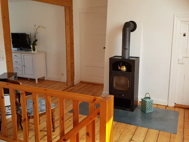 Flur Flur mit Holzdielen, Holzgeländer, schwarzem Kaminofen und Blick ins Wohnzimmer.