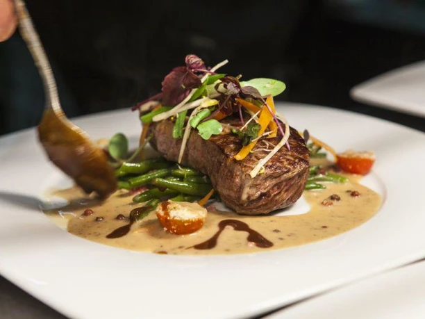 Ein saftiges Steak auf einem Bett aus grünen Bohnen, kunstvoll garniert mit frischen Kräutern.