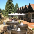 Außenansicht Restauranteingang mit Terrasse, Sonnenschirmen, Springbrunnen und einem kleinen Teich im Grünen.