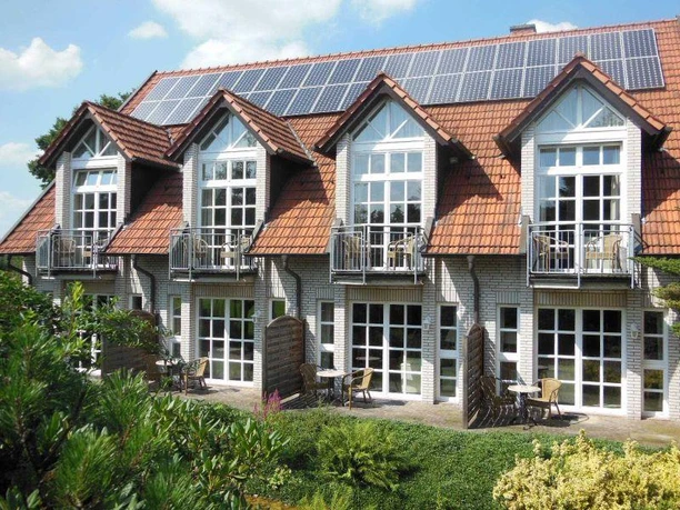 Hotel Hubertushof Das Bild zeigt ein zweistöckiges Gebäude mit Ziegeldach und weißen Fensterfronten in grüner Umgebung.