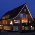 Backsteingebäude mit spitzem Giebeldach, beleuchteten Fenstern und Hotel-Restaurant-Schriftzug bei Nacht.
